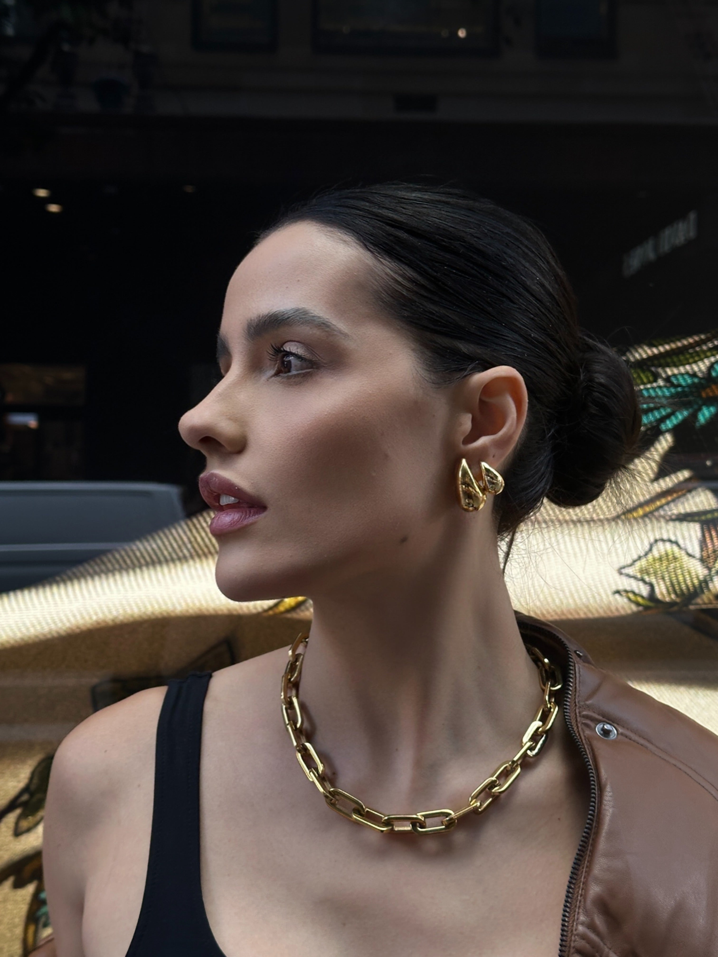 Woman wearing gold chain necklace and earrings indoors.