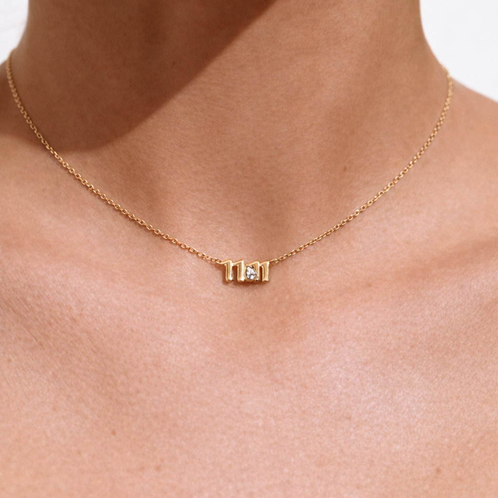 Gold necklace with a small rectangular pendant on a person's neck against a white background