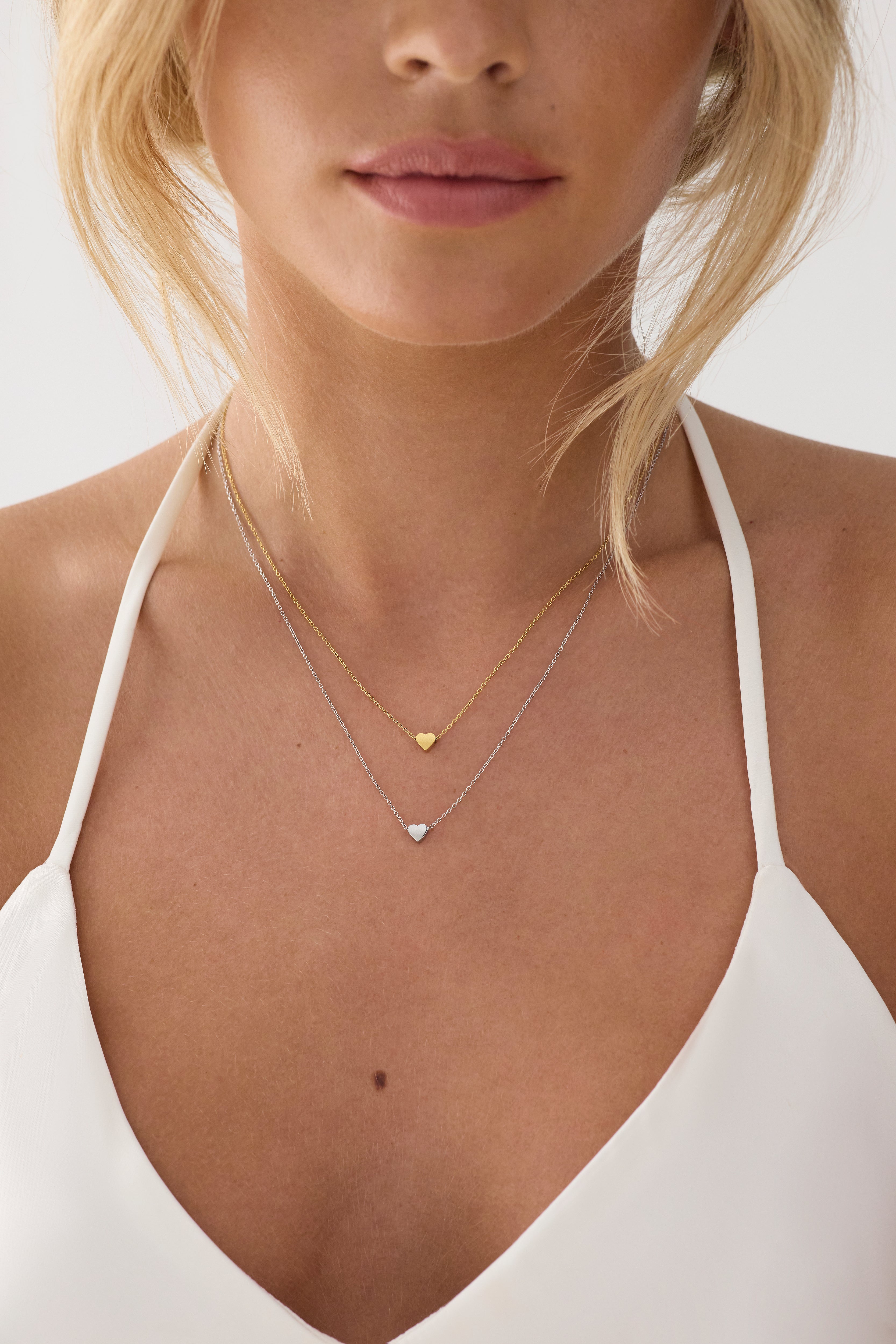 Close-up of a person wearing a gold necklace with heart pendants on a plain background