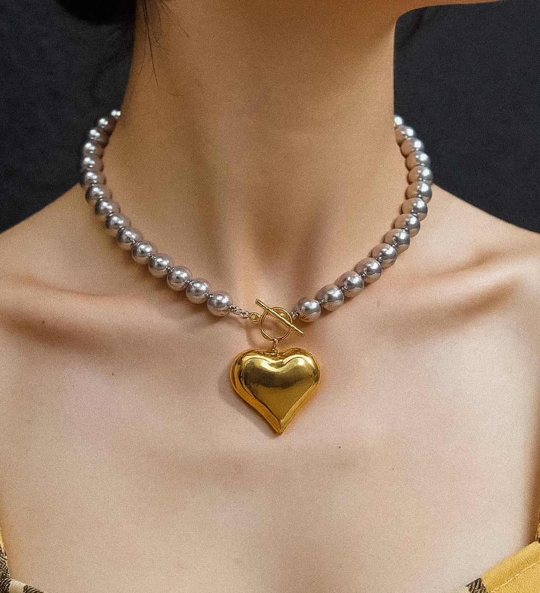 Close-up of the Ayla Necklace featuring a two-tone gold and silver heart pendant on a gold chain, displayed against a neutral background.