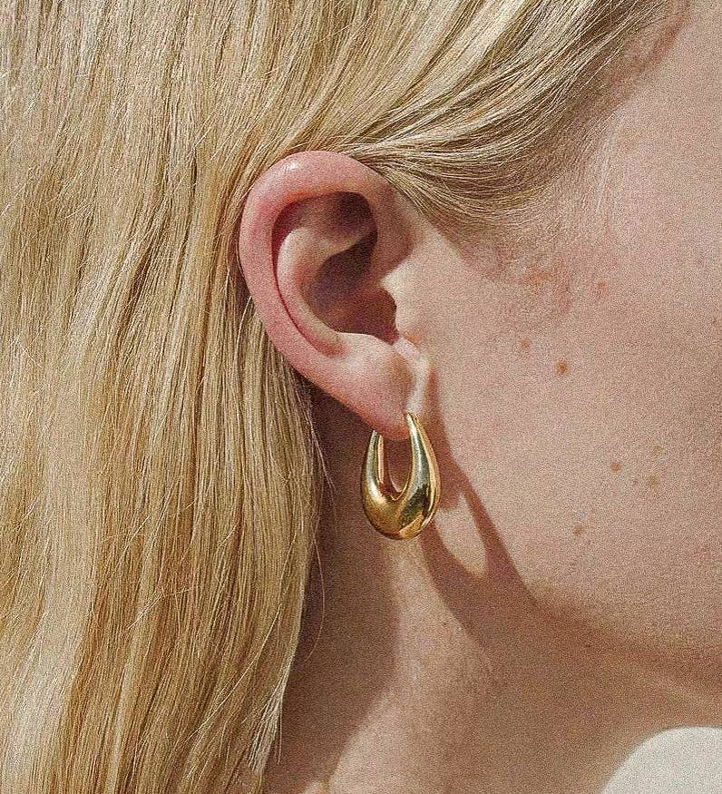 Gold droplet hoop earrings with a gently curved silhouette and smooth, polished finish. Crafted from 18K gold-plated brass, measuring 1 x 0.7 inches. Hypoallergenic, water- and tarnish-resistant—ideal for effortless everyday elegance.