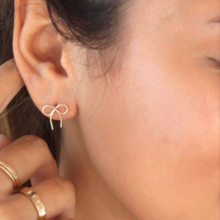 Dainty bow stud earrings crafted from 14K gold fill or sterling silver with a polished finish. Lightweight, comfortable, and hypoallergenic—perfect for adding a feminine, timeless touch to any look.