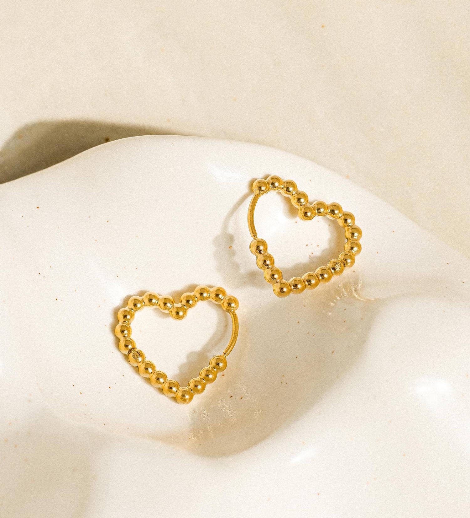Petite heart-shaped earrings crafted from 18K gold-plated stainless steel. Measuring 0.5 x 0.75 inches, these non-tarnish, hypoallergenic, lead- and nickel-free earrings are water-resistant—perfect for adding a touch of romantic charm to any look.