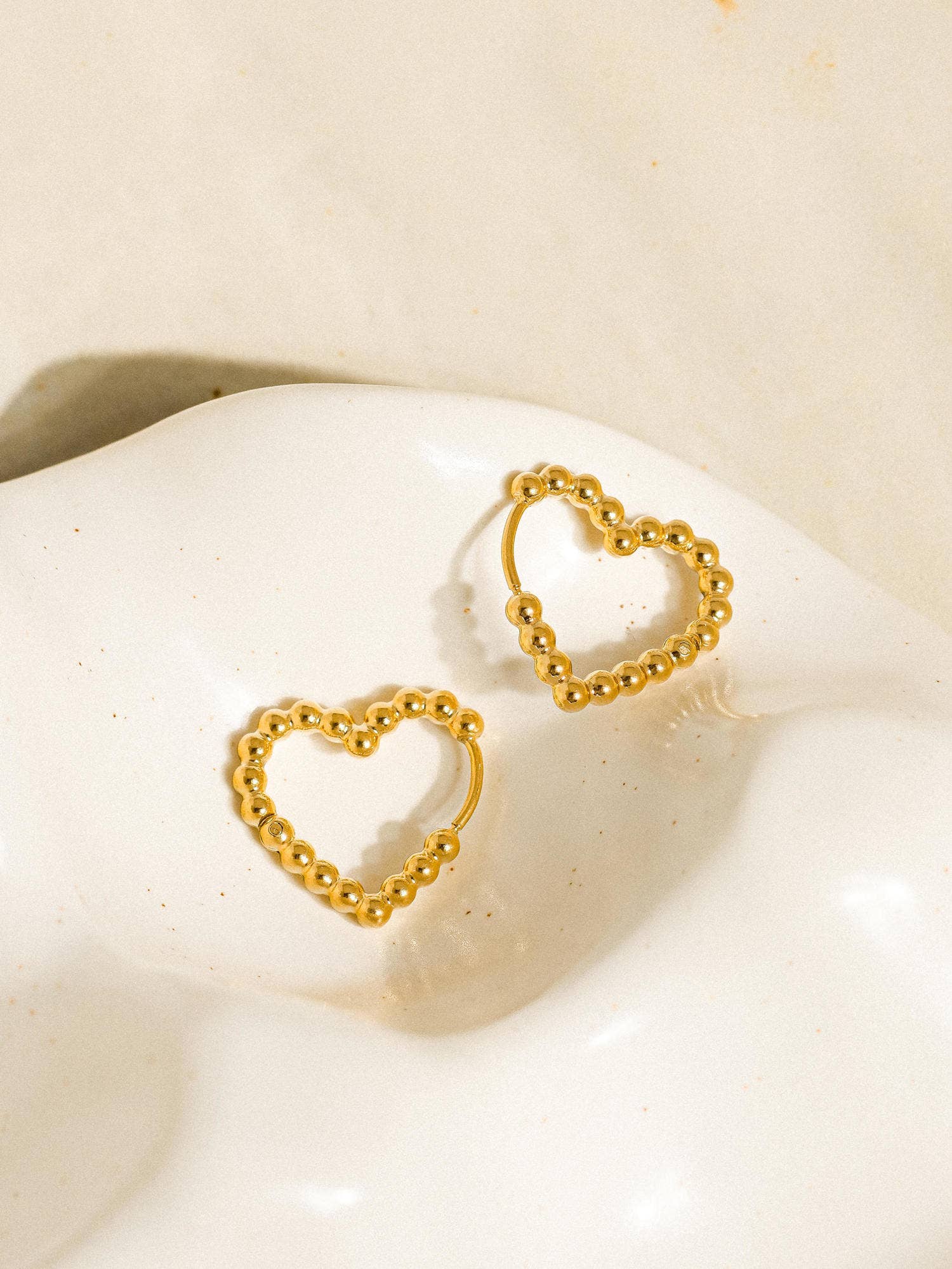 Petite heart-shaped earrings crafted from 18K gold-plated stainless steel. Measuring 0.5 x 0.75 inches, these non-tarnish, hypoallergenic, lead- and nickel-free earrings are water-resistant—perfect for adding a touch of romantic charm to any look.