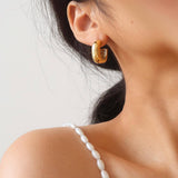 Close-up of a person wearing gold hoop earrings with a blurred background