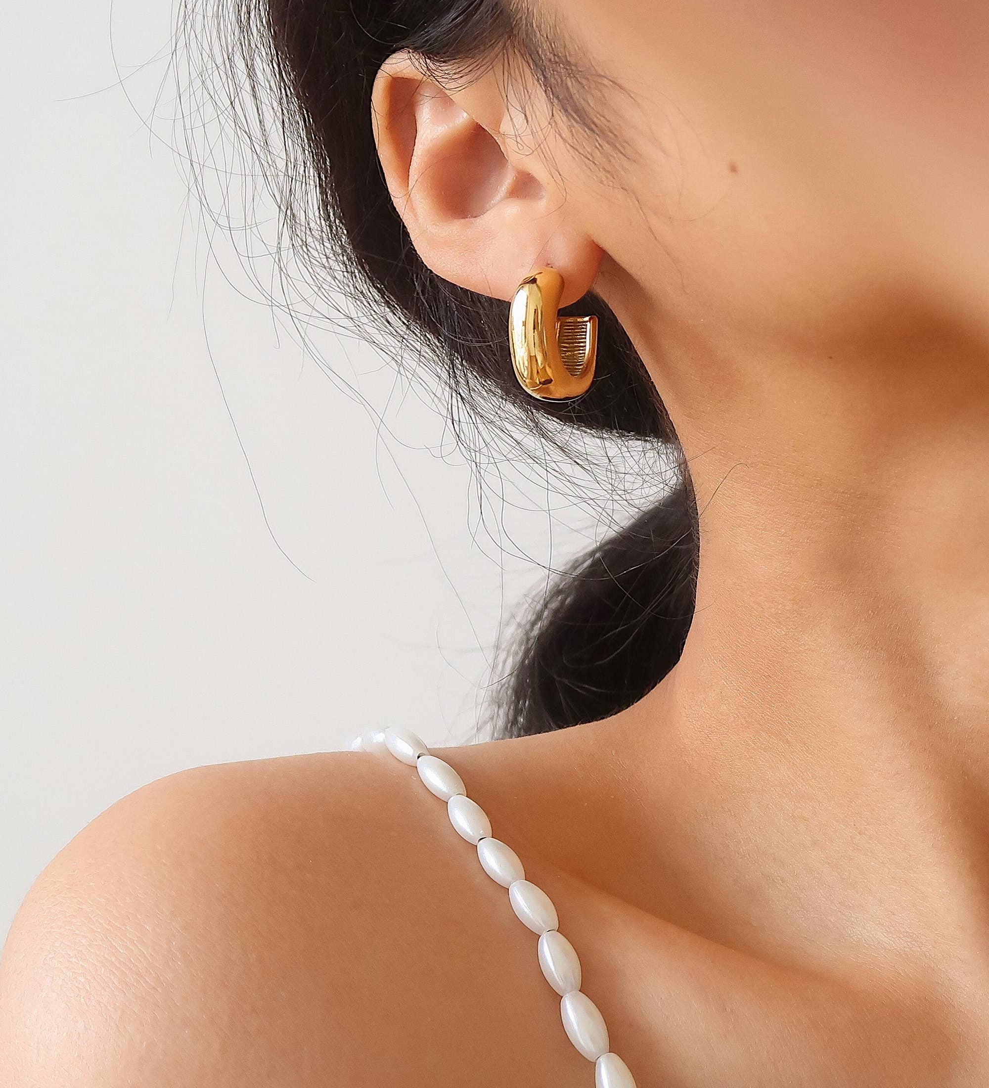 Close-up of a person wearing gold hoop earrings with a blurred background