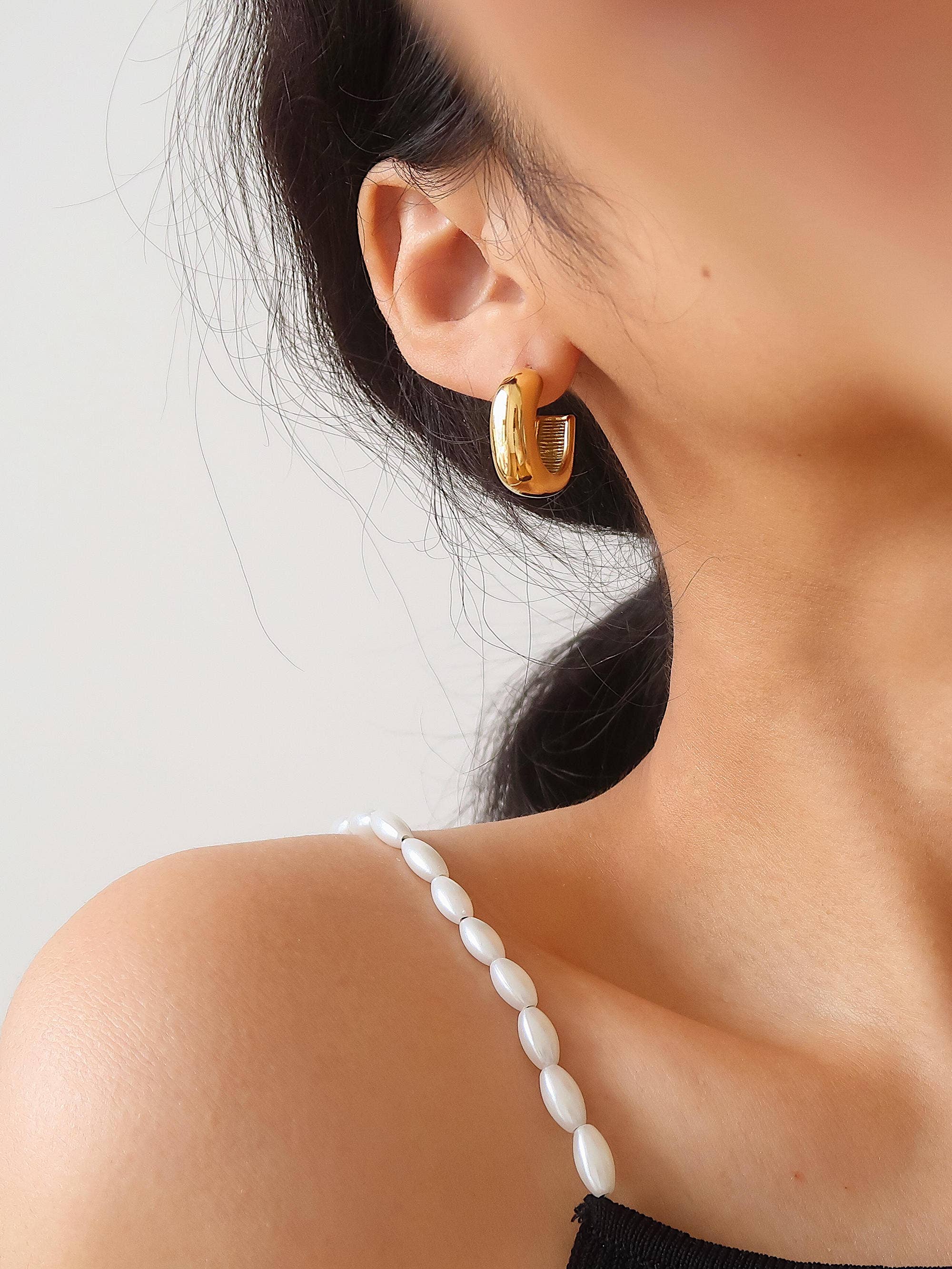 Close-up of a person wearing gold hoop earrings with a blurred background