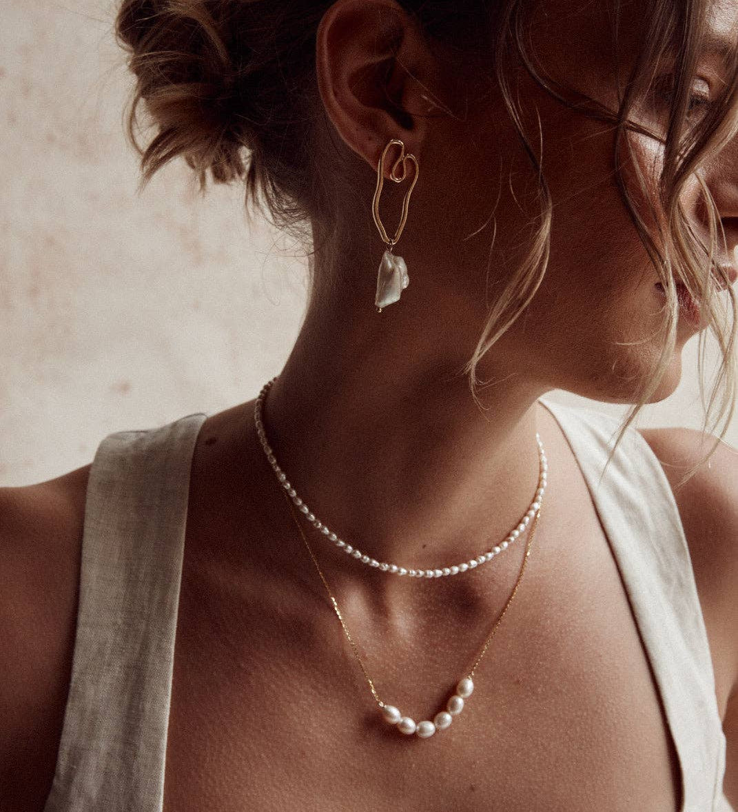 A person wearing a silver necklace with natural pearls, layered with another necklace, against a neutral background.