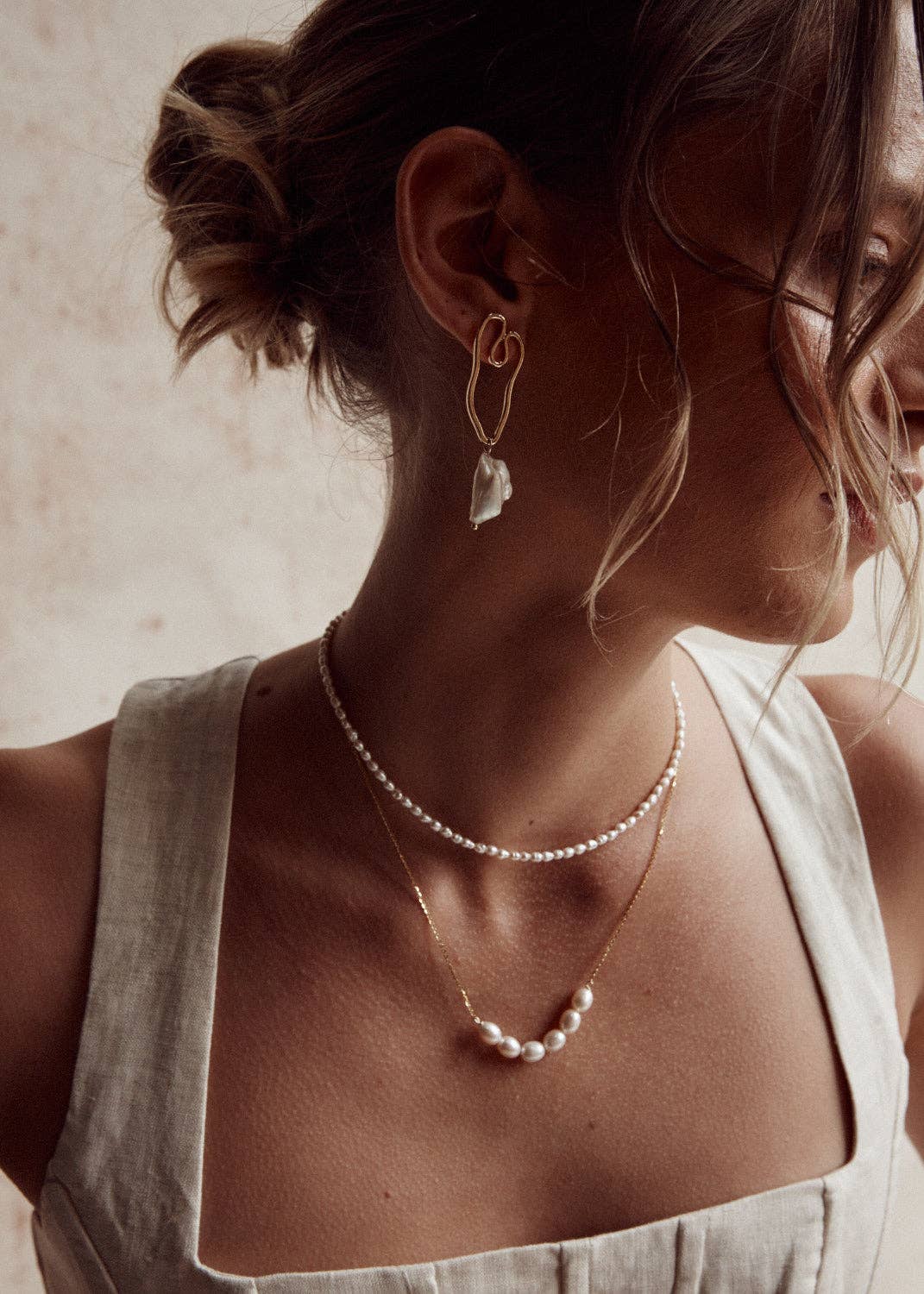 A person wearing a silver necklace with natural pearls, layered with another necklace, against a neutral background.
