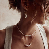 A person wearing a silver necklace with natural pearls, layered with another necklace, against a neutral background.