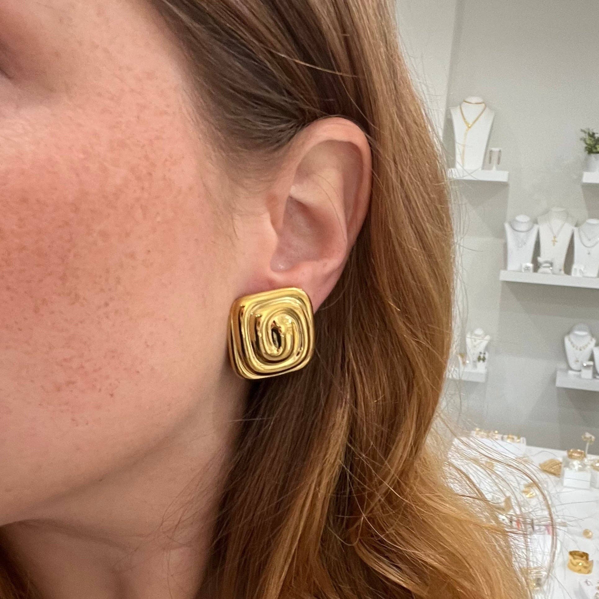 Matilda Swirl Stud Earrings in 18K gold plated stainless steel, featuring a sculptural twisted swirl design with a 1-inch diameter, styled by a model. 