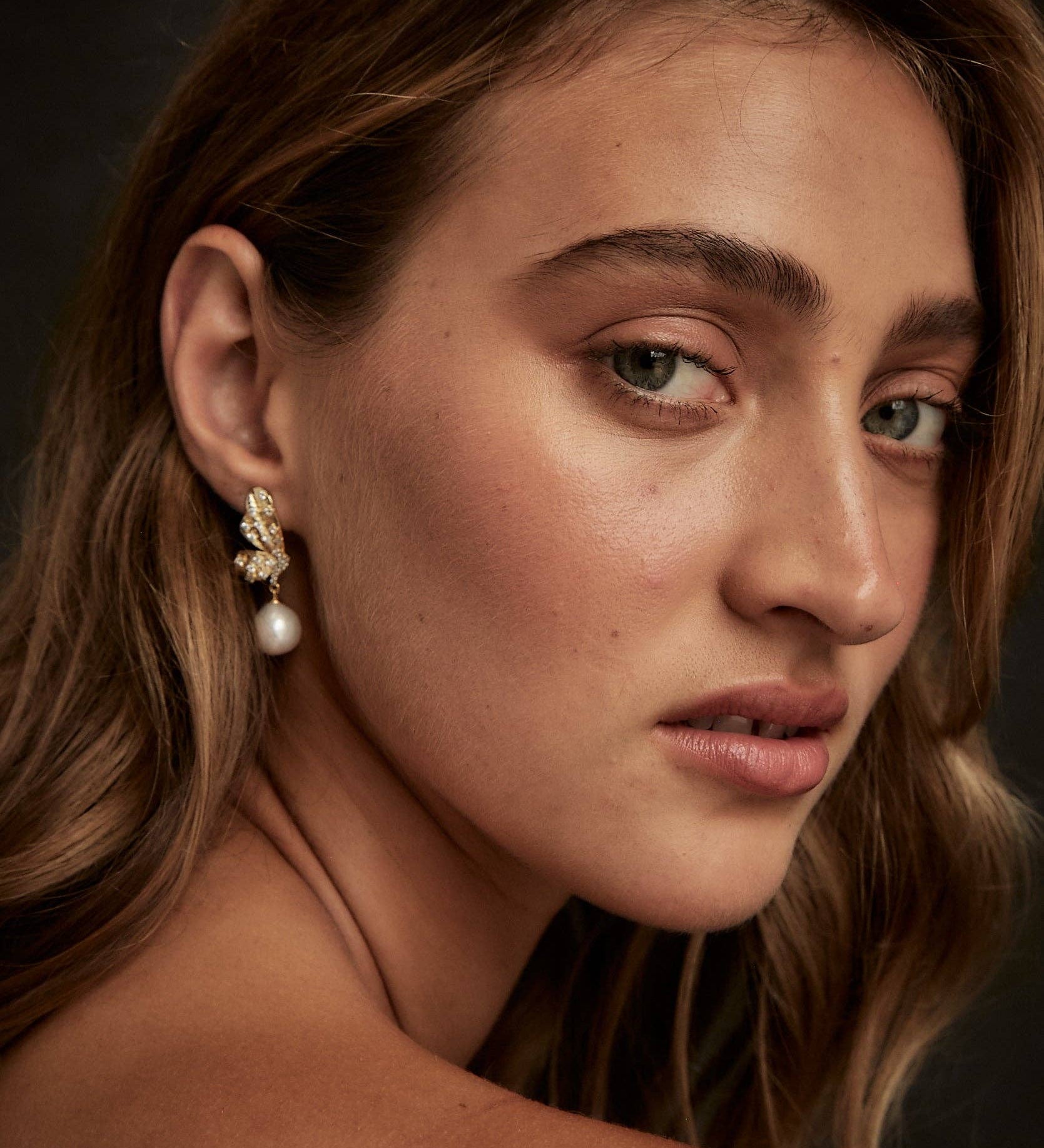 A woman showcasing silver and gold-plated winged pearl earrings with cubic zirconia stones.