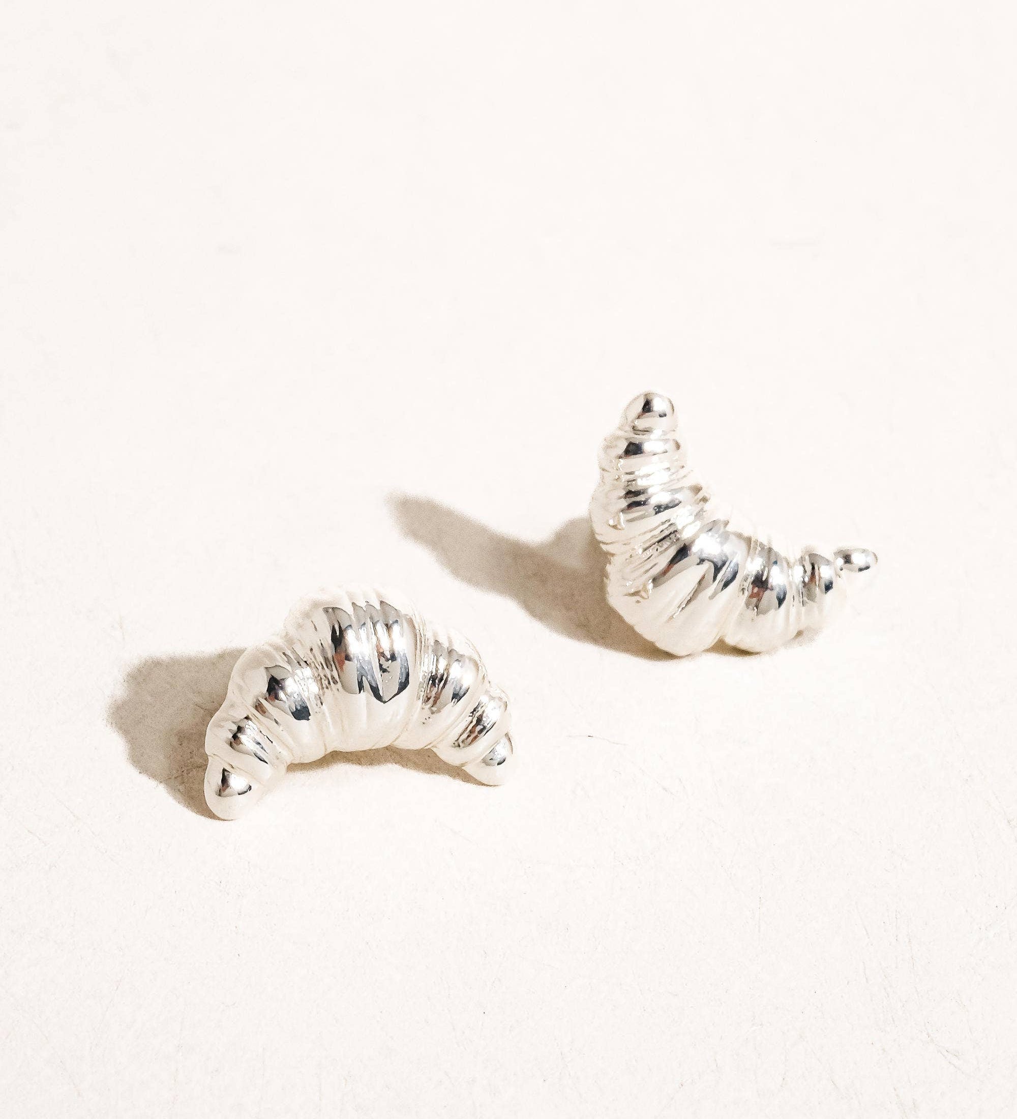 Petite sculptural stud earrings crafted from a brass base with premium 18K gold or silver plating, featuring a modern croissant-inspired design. Minimalist and Parisian-chic—perfect for adding a stylish twist to any everyday look. Hypoallergenic, water- and tarnish-resistant.