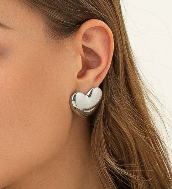 Silver heart-shaped stud earrings on model. 