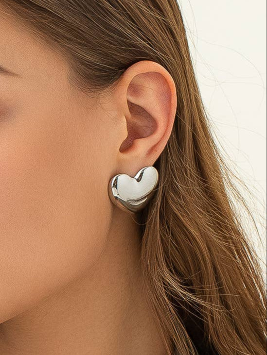 Silver heart-shaped stud earrings on model. 