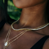 Elegant tennis necklace featuring a continuous line of sparkling cubic zirconia stones set in 18K gold-plated stainless steel. Designed for timeless sparkle with a modern edge, this hypoallergenic, water- and tarnish-resistant piece is perfect worn solo or layered for added glamour.